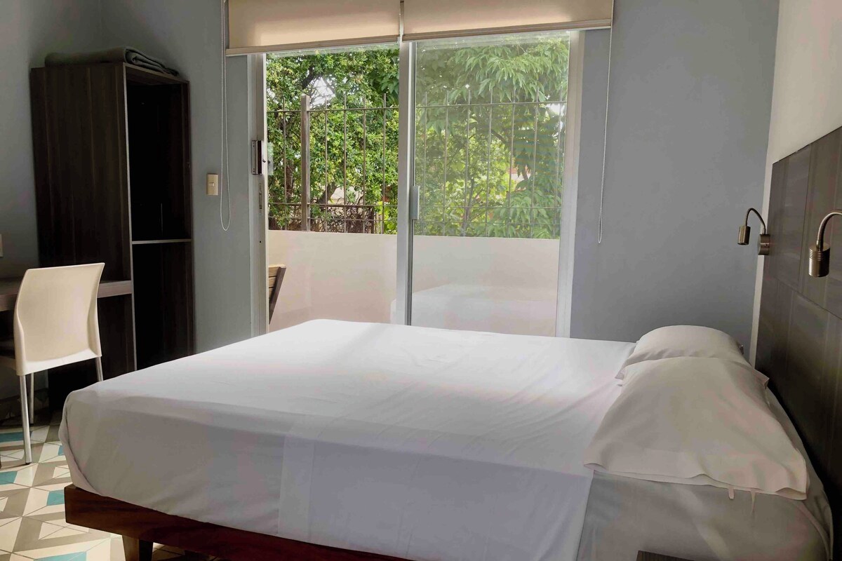 Un dormitorio con cama, una silla, armario y puerta corrediza de vidrio que da a un espacio exterior.