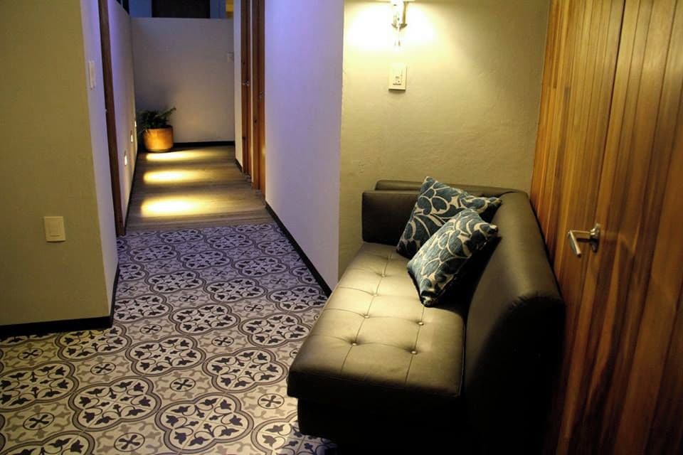 A hallway with patterned flooring, a sofa with patterned cushions, and a wall-mounted light fixture.