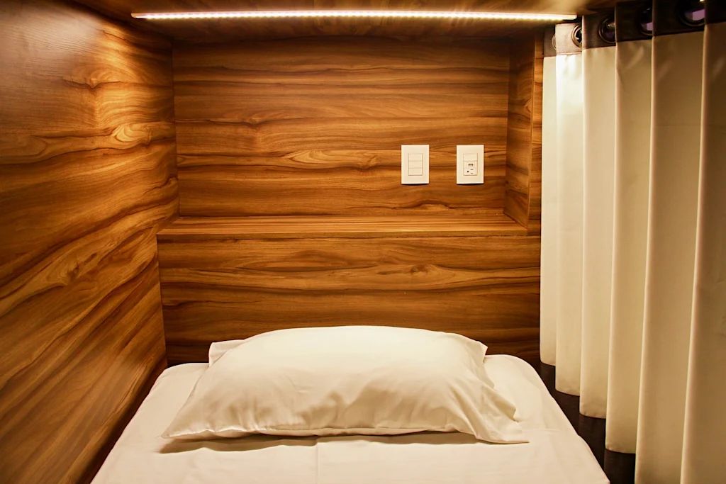 Una habitación pequeña y acogedora con paredes de madera, una cama individual con almohada blanca y un interruptor de luz en la pared.