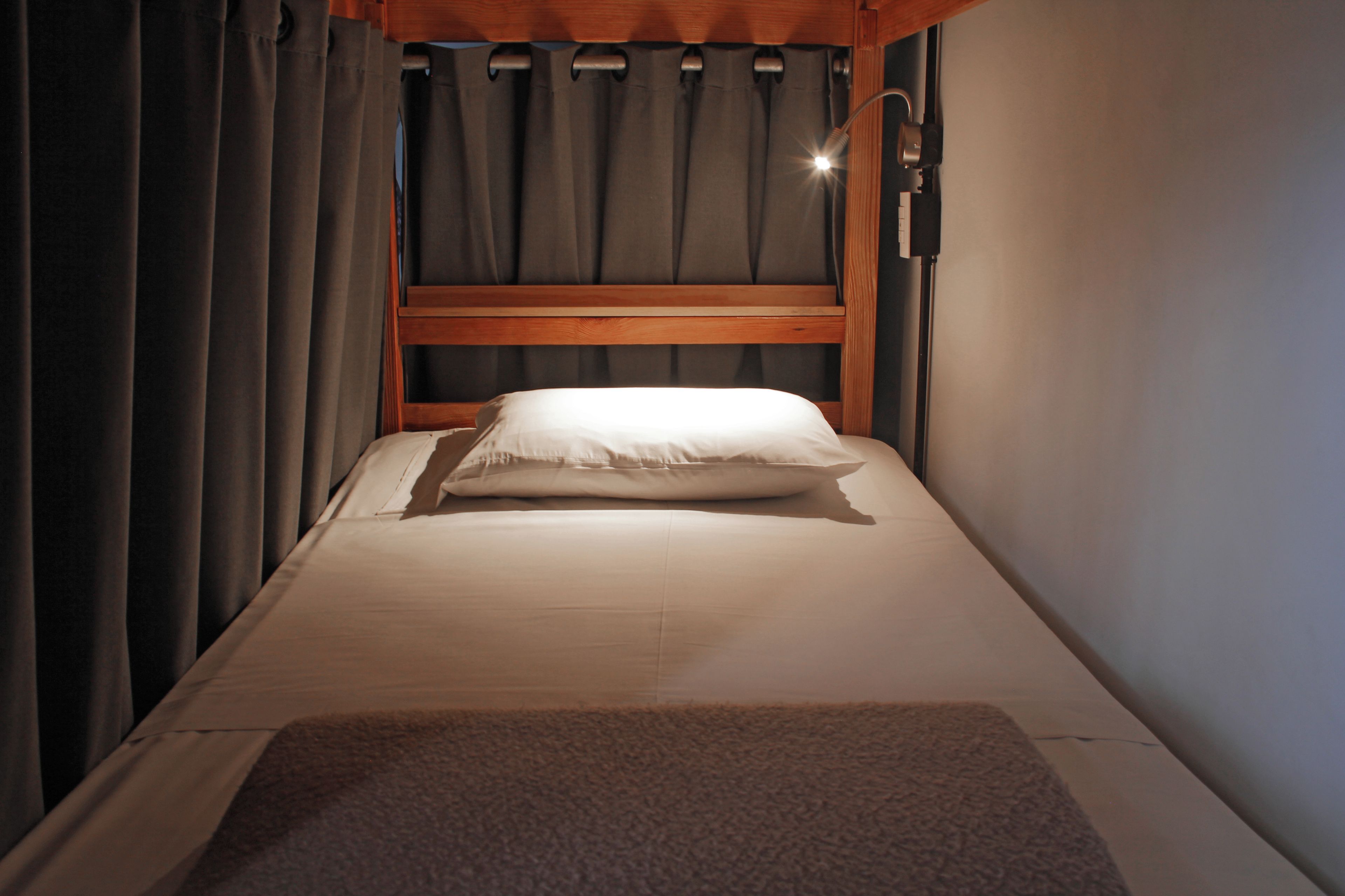 A single bed with a wooden headboard, a white pillow, and a brown throw blanket.