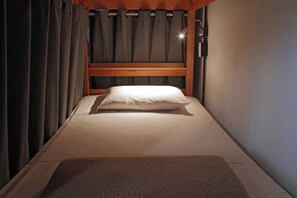 Una cama individual con cabecera de madera, almohada blanca y manta marrón.