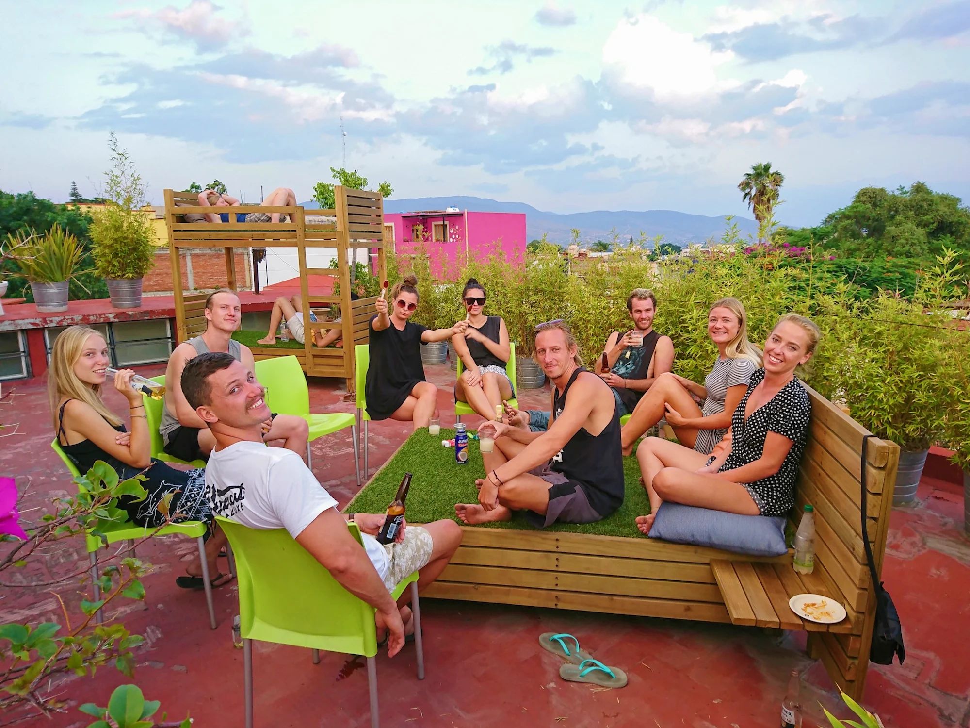 Un grupo de personas sentadas en un banco y sillas en una terraza en la azotea, con vistas a zonas verdes y edificios al fondo.