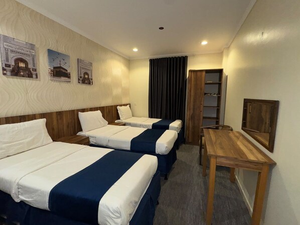 A hotel room with two beds, a wooden table, a wardrobe, and a mirror on the wall.