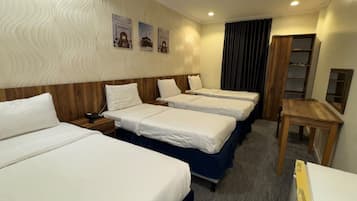 A hotel room with three beds, a wooden headboard, a desk, and a small table.