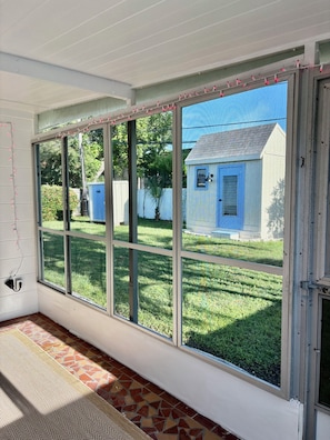 A room with a large window overlooking a backyard, a tiled floor, and a door with a latch. - Modern Cozy 2BR-2BA Casita - Pet Friendly, dog- 5 min to Madeira Beach, (ST. PETERSBURG)