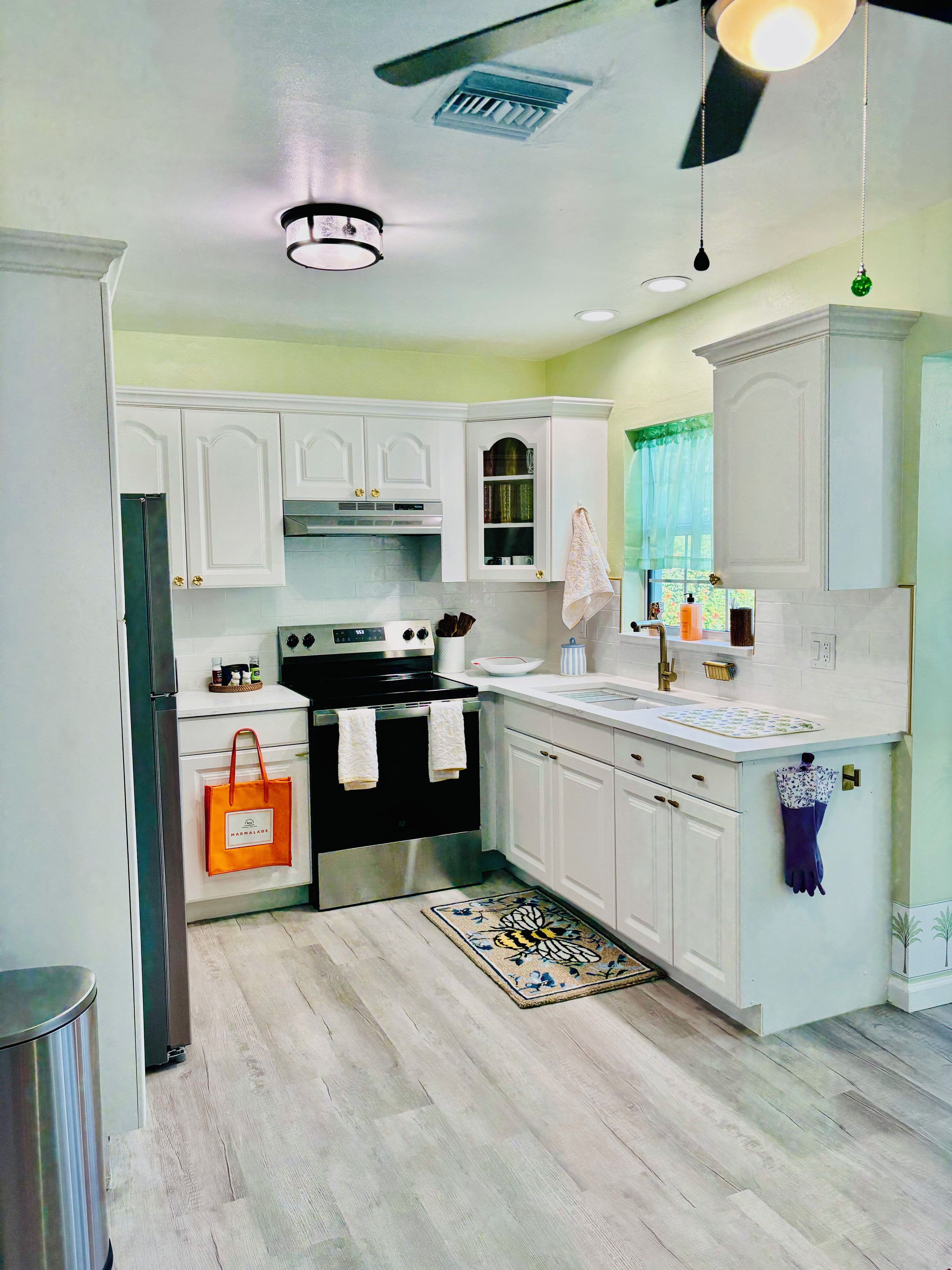 A modern kitchen with white cabinetry, a stainless steel stove, and a wooden floor.