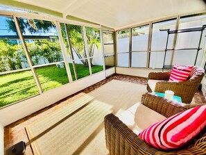 A sunlit room with wicker furniture, large windows, and a view of a green garden.