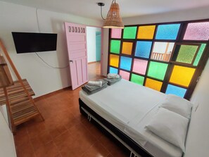 A bedroom with a bed, a wooden staircase, a pink door, and a colorful window.