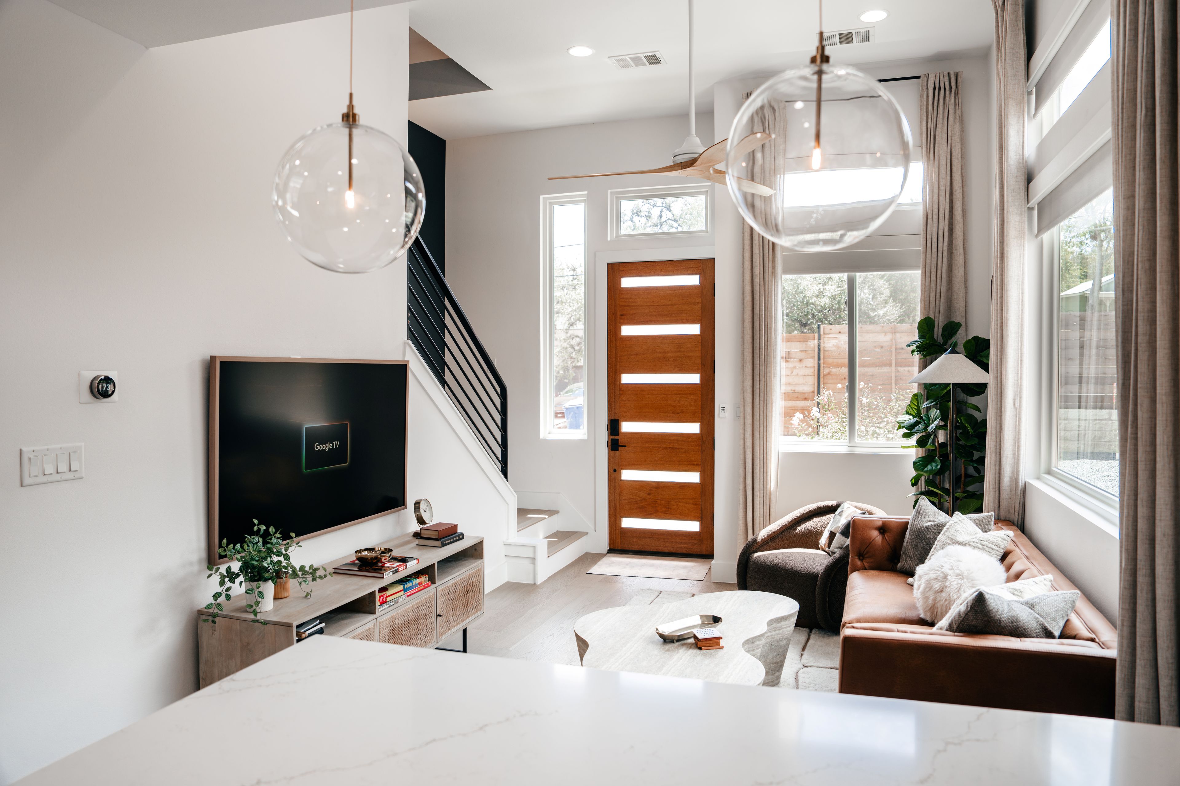 A modern living room with a flat-screen TV, a staircase, and a large window with curtains.