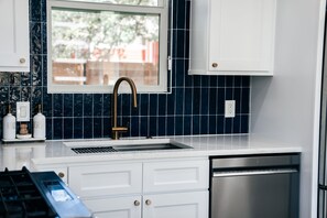 A kitchen with white cabinets, a stainless steel dishwasher, and a window with a view of greenery outside. - Newly remodeled 2br/2ba on South First! OleMiss + F1! (Austin)