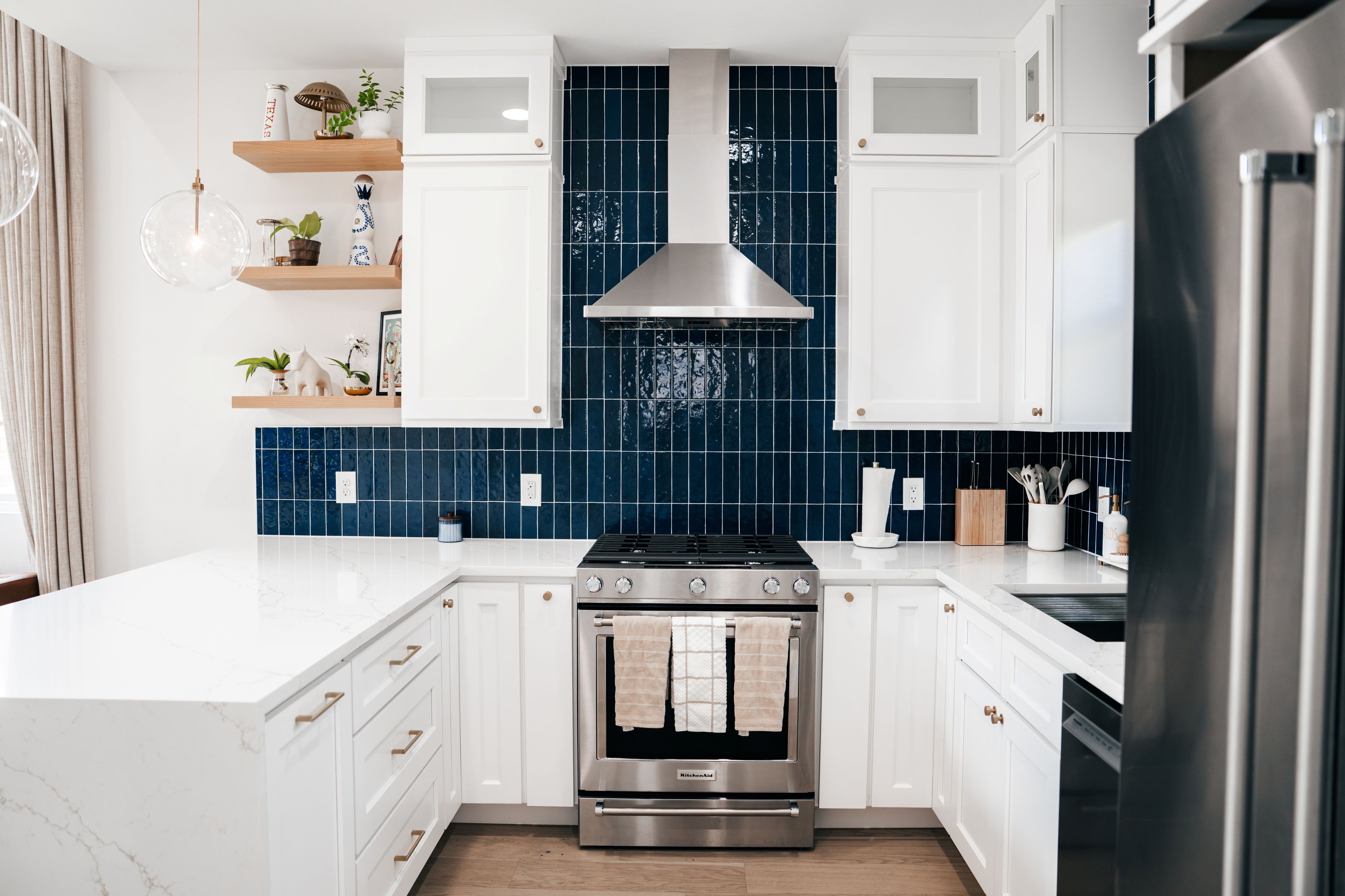 Una cocina moderna con armarios blancos, estufa de acero inoxidable y salpicadero de azulejos azules.