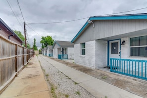 A row of single-story houses with blue trim and white exteriors, a wooden fence on the left, and a gravel pathway. - Near Texans | NRG Stadium | Med Center | Downtown! (Houston)