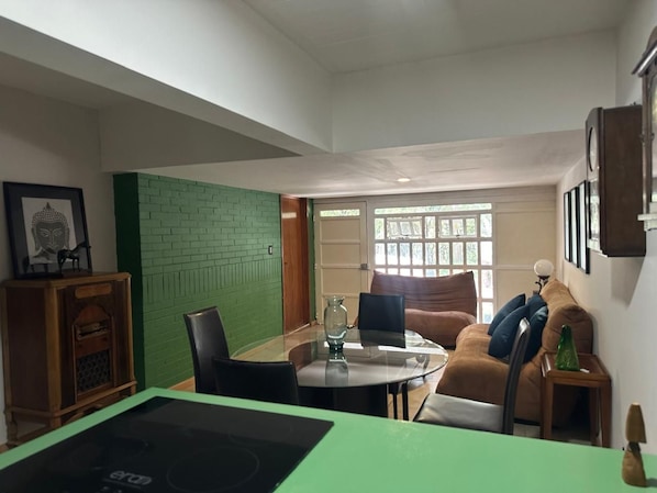 A room with a dining table, chairs, a sofa, and a green accent wall.