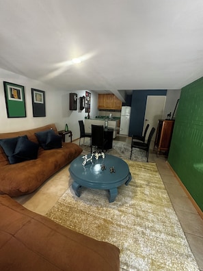 A living room with a brown sofa, a blue coffee table, and a kitchen in the background.
