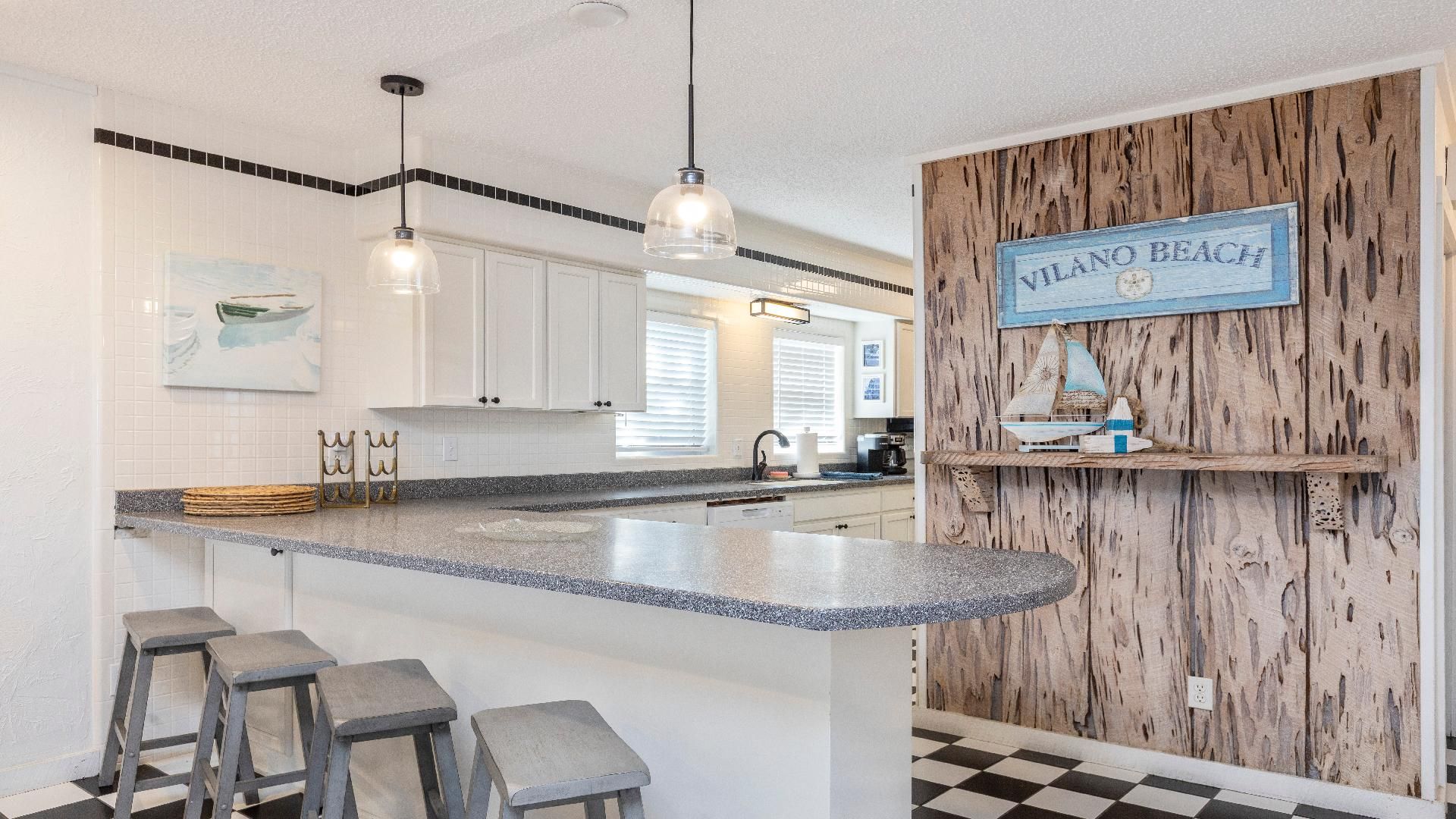 A kitchen with a central island, bar stools, pendant lights, and a wooden accent wall with a 'Vilano Beach' sign.
