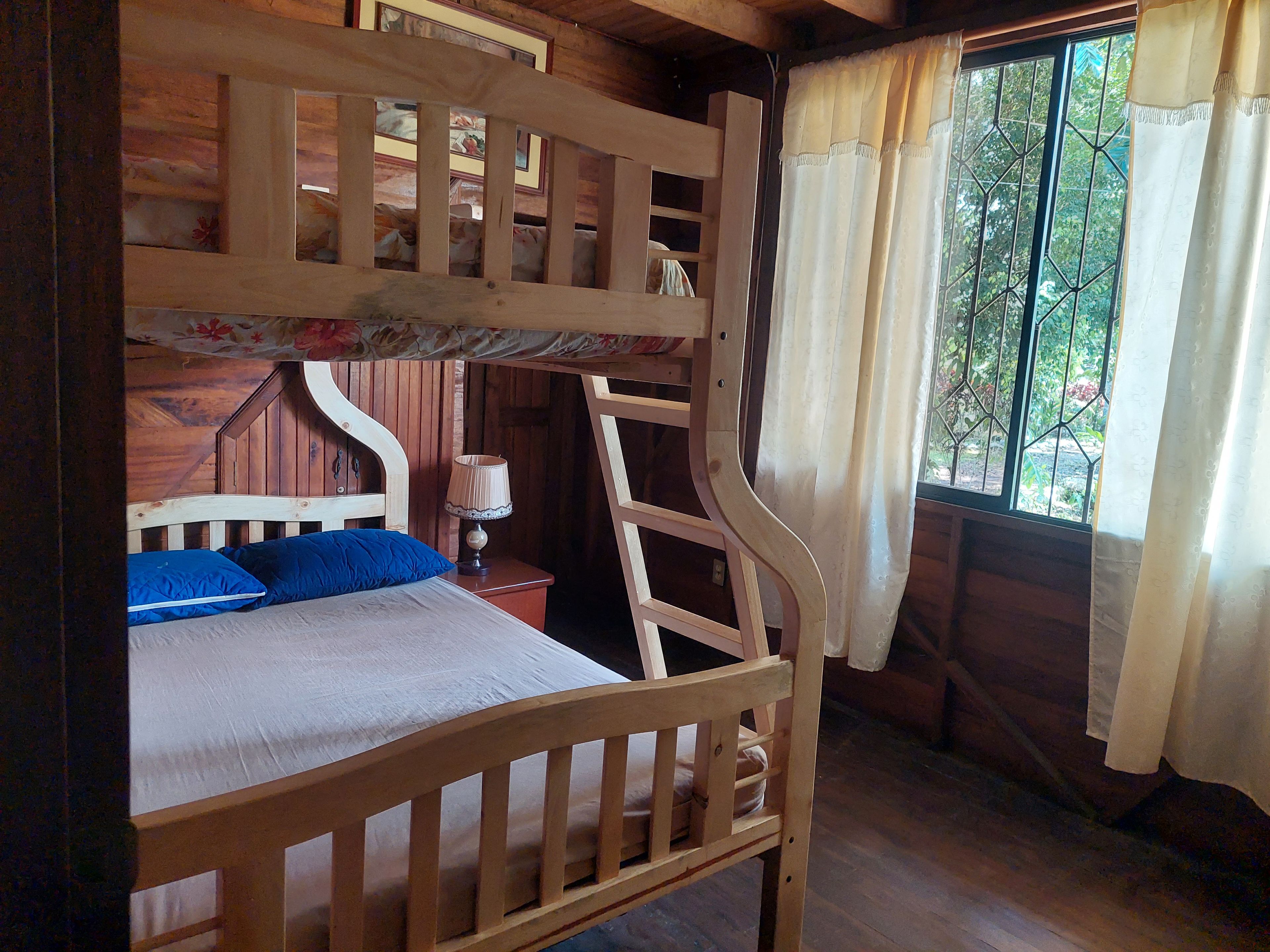 Un lit superposé avec une structure en bois, une table de chevet avec une lampe et une fenêtre avec des rideaux.