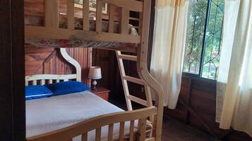 A bunk bed with a wooden frame, a bedside table with a lamp, and a window with curtains.