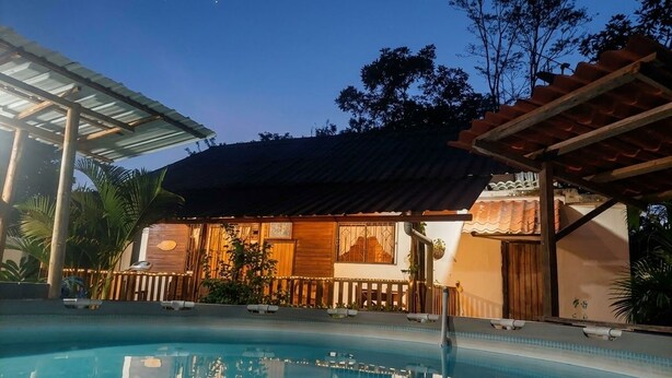 A poolside area with a house in the background, a covered patio, and a clear sky. - Your Amazonian retreat, private pool, and nature (Tena)