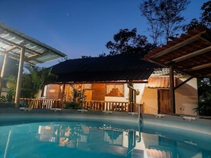 A poolside area with a house in the background, a covered patio, and a clear sky.