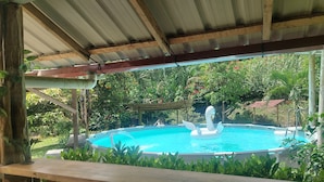 A swimming pool with a swan floatation device, surrounded by lush greenery and a wooden deck. - Your Amazonian retreat, private pool, and nature (Tena)