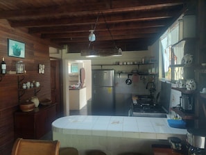 A rustic kitchen with wooden beams, a refrigerator, a stove, and various kitchen utensils.