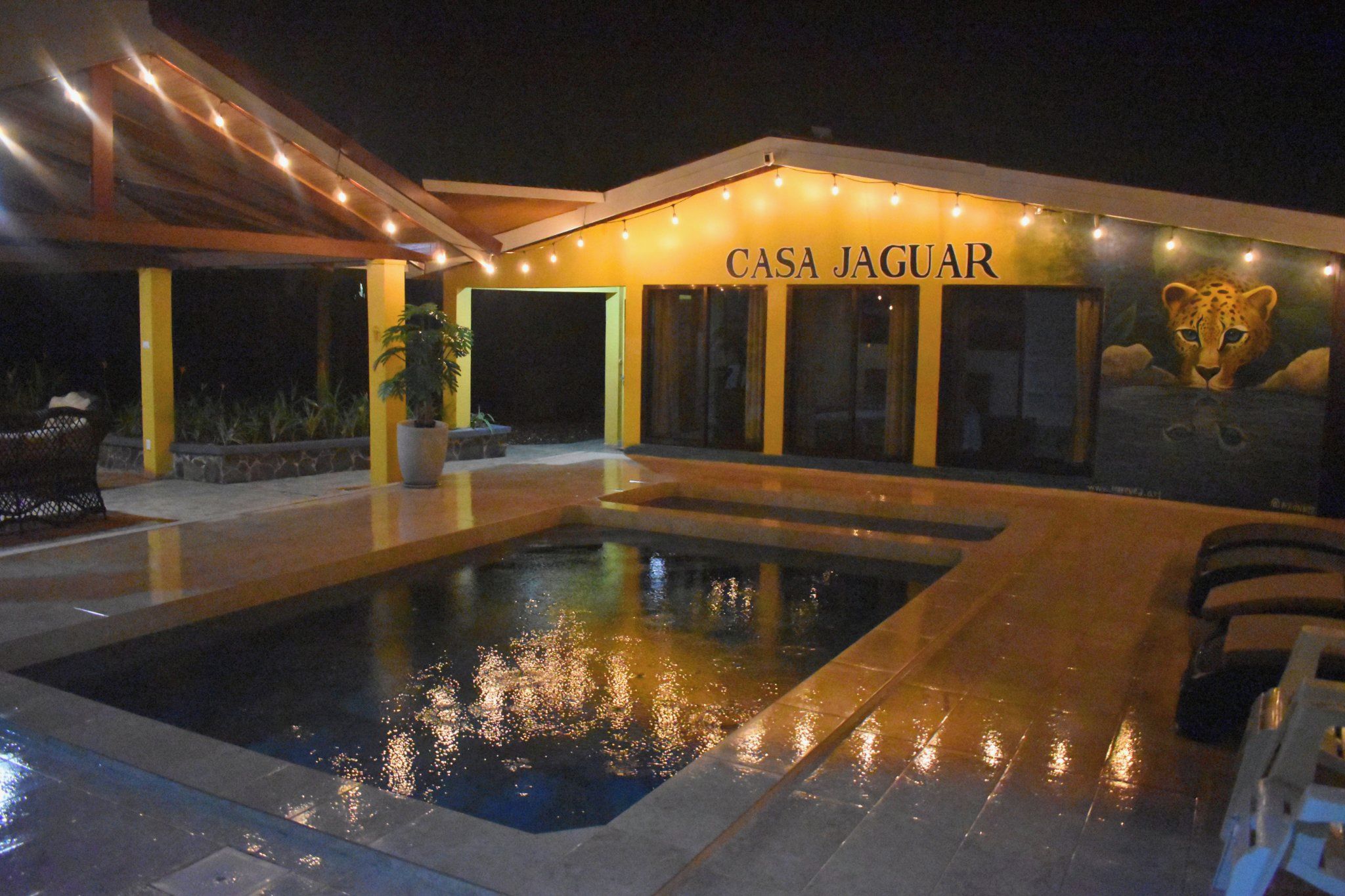 Un espace piscine avec un bâtiment portant l’inscription « CASA JAGUAR » et une fresque représentant un guépard.