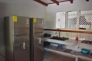 Een kleine keuken met een roestvrijstalen koelkast, een spoelbak met een kraan en een raam met een traliewerk.