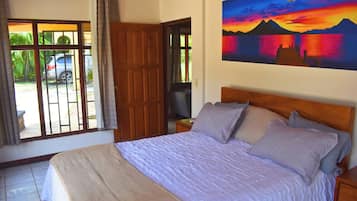 Une chambre à coucher avec un lit, un tableau, une télévision et une vue sur une voiture garée à l’extérieur.