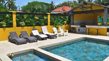 Une piscine avec des chaises longues et un espace barbecue.