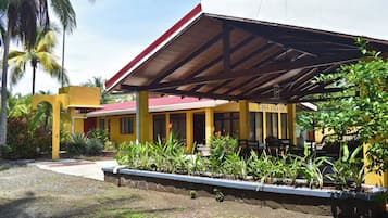 Un bâtiment jaune avec un toit rouge, portant l’inscription « CASA JAGUAR », entouré de plantes tropicales et de palmiers.