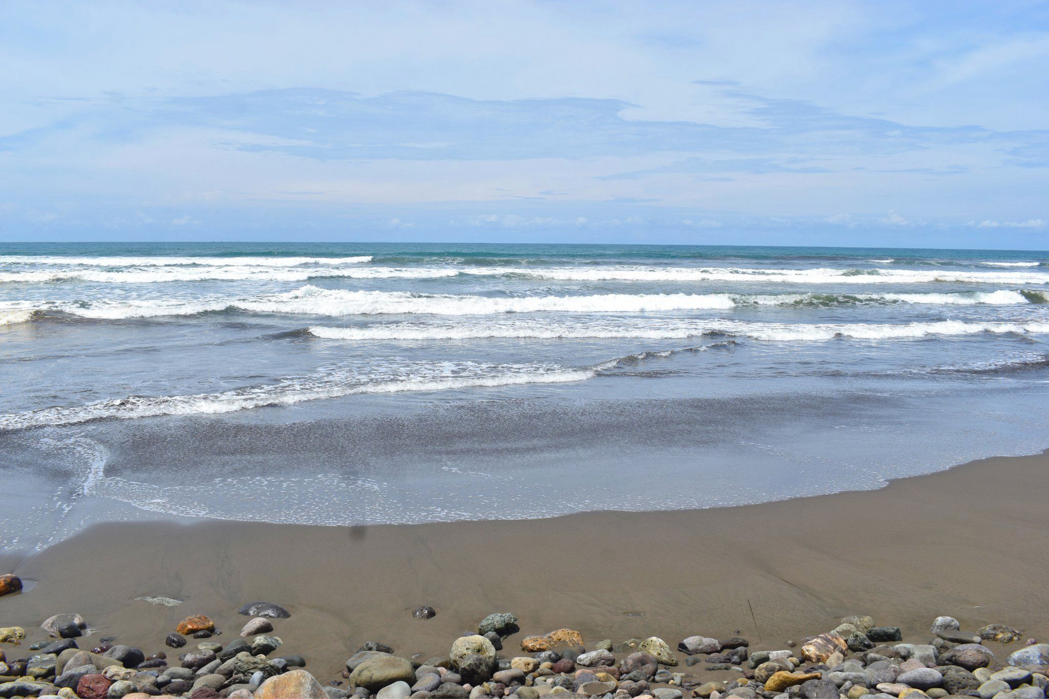 Una playa con olas, piedras y cielo despejado.