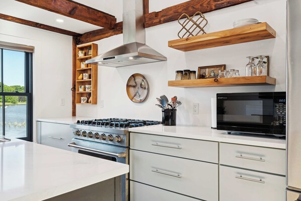 A modern kitchen with a gas stove, a microwave, wooden shelves, and a view of the outdoors.