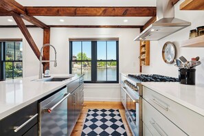 A modern kitchen with a large window, wooden beams, and a view of a body of water. - Kimball Island | River Views | Walk Downtown (Exeter)