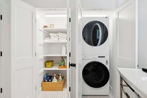 A compact laundry room with a washing machine, a dryer, and neatly organized shelves with towels and cleaning supplies.