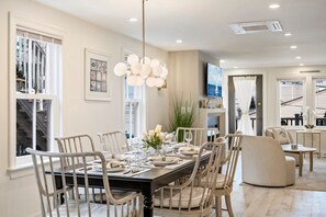 A dining area with a black table set for six, surrounded by white chairs with cushioned seats. - Coastal Grand Koz | Steps to Beach | Ocean View (Salisbury)