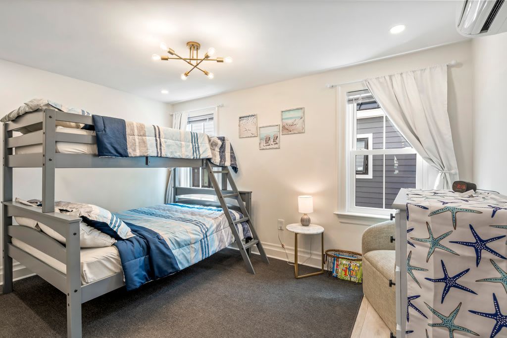 A bunk bed room with a ladder, a small table with a lamp, and a chair with star-patterned upholstery.