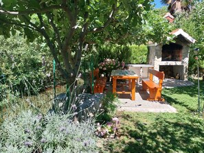 An outdoor seating area with a stone table and chairs, surrounded by lush greenery and a small garden. - Kuča na rjeci s velikim vrtom I pogledom na planine,3km od mora - Split 10km. (Žrnovnica)