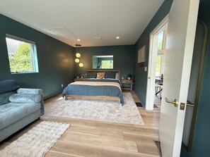 A bedroom with a bed, bedside tables, a sofa, and a door leading to another room. - Bloom On The Spring: A modern Retreat in Nature. (Chambersburg)