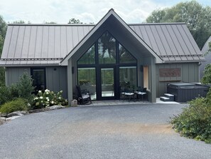 A modern building with a large glass entrance, outdoor seating, and a hot tub. - Bloom On The Spring: A modern Retreat in Nature. (Chambersburg)