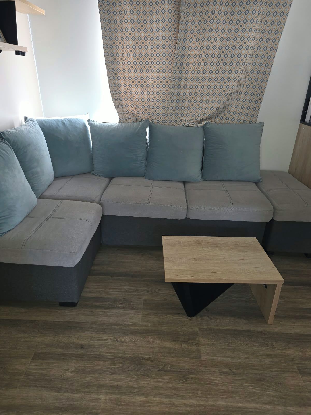 A modern living room with a sectional sofa, a wooden coffee table, and a patterned curtain.