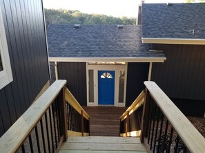 A wooden staircase leading to a blue door with a window, surrounded by dark siding and a sloped roof. - Home on the Cove is lakefront with a private dock (Sunrise Beach)