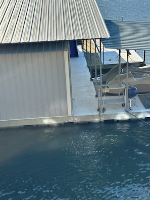A boat docked at a pier with a metal roof and a concrete walkway leading to the water. - Home on the Cove is lakefront with a private dock (Sunrise Beach)
