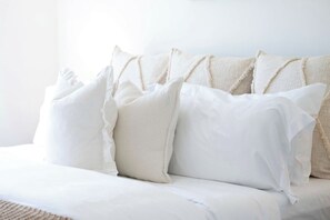 Un lit avec une literie blanche et plusieurs oreillers.