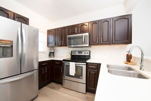 A modern kitchen with stainless steel appliances, dark wooden cabinets, and a double sink. - Beach Living at Plantation Village BLD (George Town)