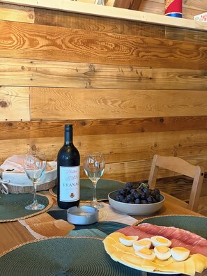 A wooden table with a bottle of wine, two glasses, a bowl of grapes, and a plate of food.