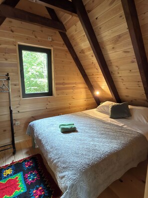 A bedroom with a wooden ceiling, a window, a bed with white bedding, and a colorful rug.