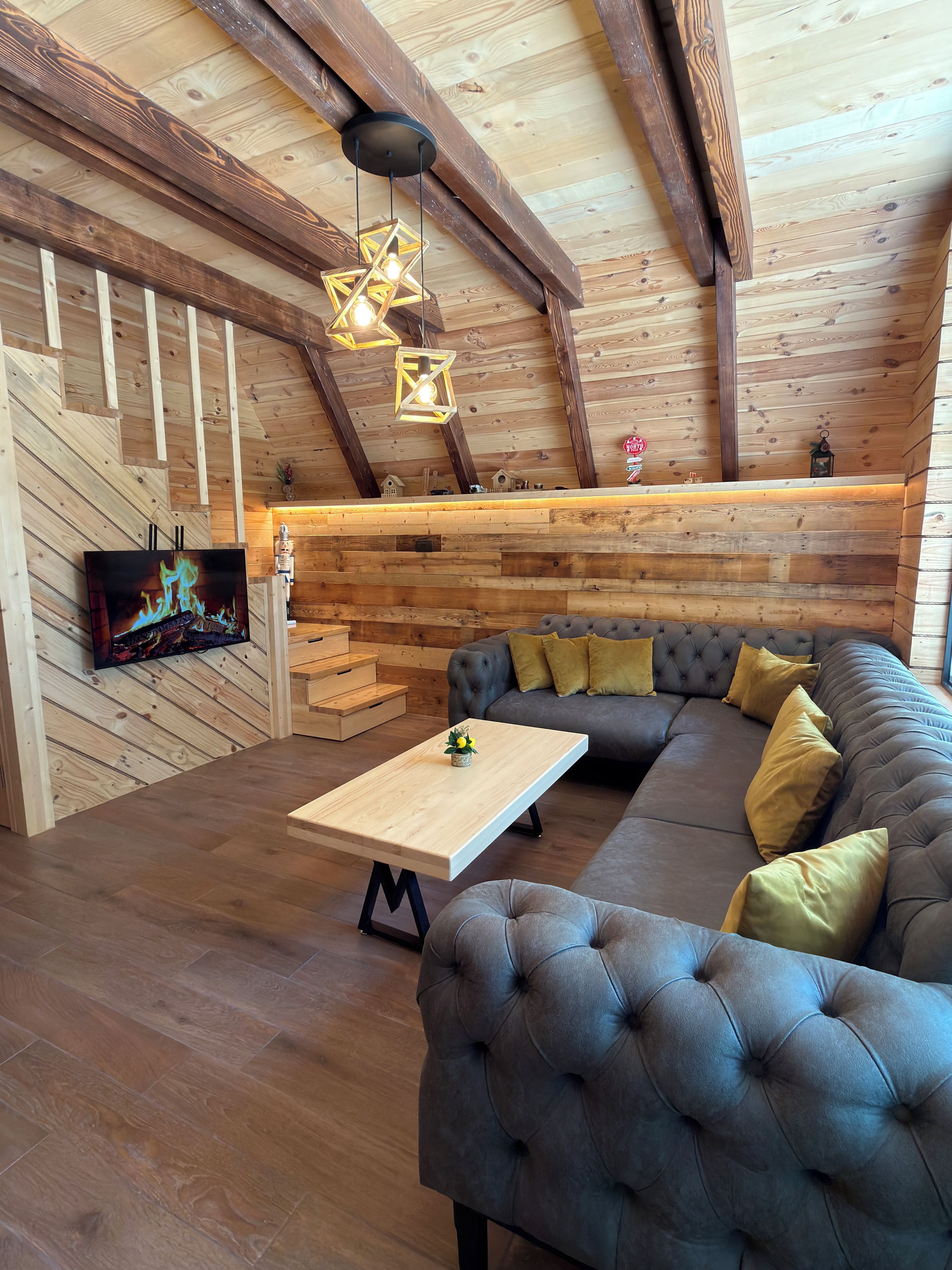 A cozy living room with a sectional sofa, a flat-screen TV, wooden beams, and a star-shaped hanging light fixture.