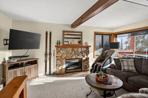 A living room with a stone fireplace, a flat-screen TV, a sofa, and a massage chair. - Big White Ski-In/Ski-Out Townhome | Private Hot Tub + Mountain Views (Kootenay Boundary E / West Bo*)