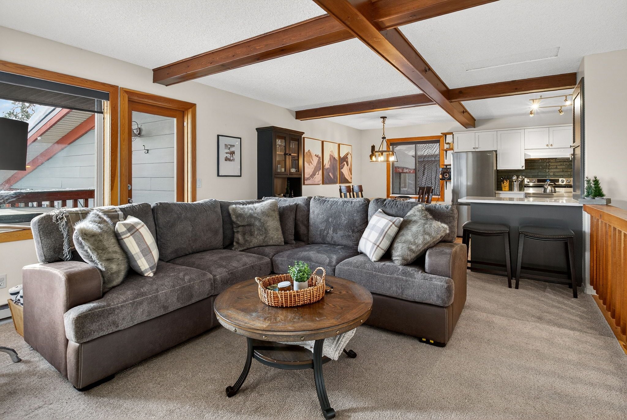 A modern living room with a sectional sofa, a coffee table, and a kitchen area with a refrigerator and bar stools.