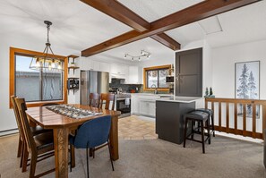A spacious kitchen with a dining area, wooden beams, and a view through a window. - Big White Ski-In/Ski-Out Townhome | Private Hot Tub + Mountain Views (Kootenay Boundary E / West Bo*)